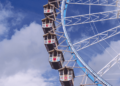 Ferris wheel with colorful gondolas against a cloudy blue sky.