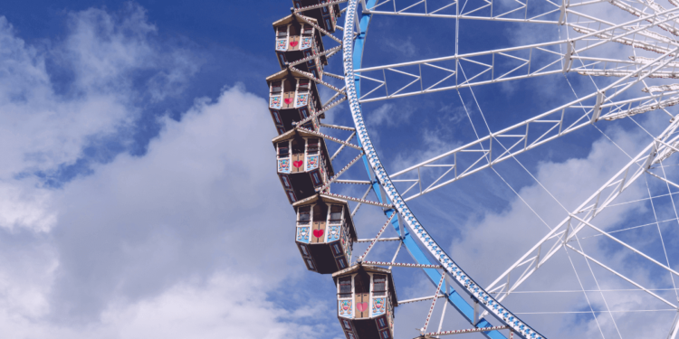 Ferris wheel with colorful gondolas against a cloudy blue sky.