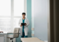 Doctor in a white coat standing in a medical office, reading a tablet.