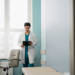 Doctor in a white coat standing in a medical office, reading a tablet.