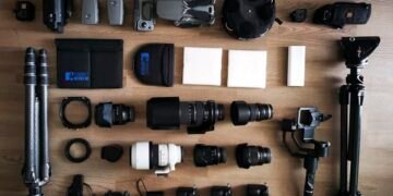 Aerial view of arranged photography equipment on a wooden floor, including cameras, lenses, drones, tripods, and accessories.