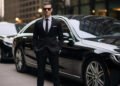 Man in a suit standing beside black luxury cars.