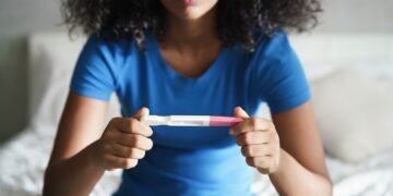 Disappointed hispanic girl getting unexpected result from pregnancy test kit. Sad young latina woman sitting alone on her bed.