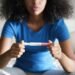 Disappointed hispanic girl getting unexpected result from pregnancy test kit. Sad young latina woman sitting alone on her bed.