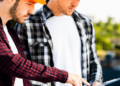 Two men in hard hats examining a tablet, discussing plans on a construction site.