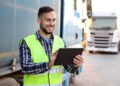 Truck driver in front of his trucks. About 30 years old, smiling Caucasian mid adult man.