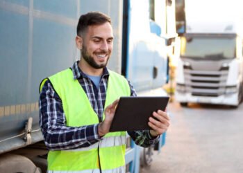 Truck driver in front of his trucks. About 30 years old, smiling Caucasian mid adult man.