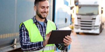 Truck driver in front of his trucks. About 30 years old, smiling Caucasian mid adult man.